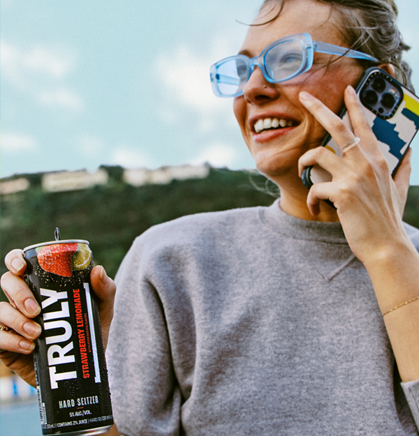 Woman holding a can of Truly Strawberry Lemonade and talking on a smart phone