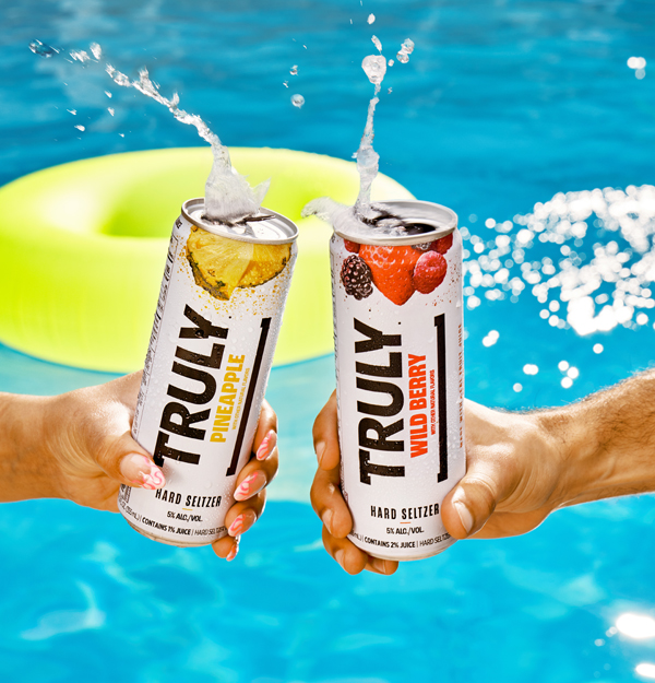 Two hand cheers-ing with Truly Hard Seltzer against a pool backdrop